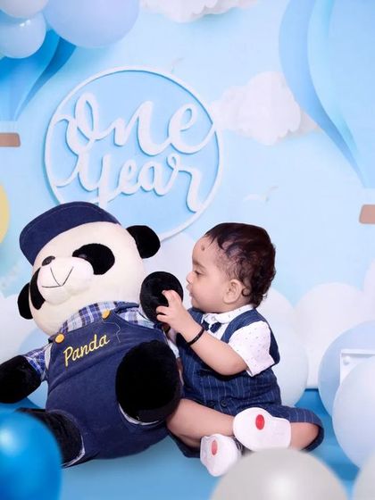 A creative shot for a first birthday. The baby boy plays with a panda toy in a beautifully arranged blue and white themed setup, marking his 'One Year' milestone.