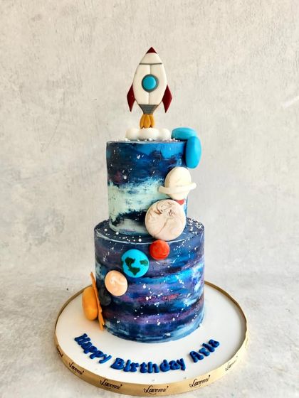 A galaxy-themed cake for Arla's birthday. The two tiers are hand-painted to look like a nebula, with a rocket blasting off from the top.