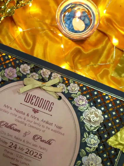 The warm glow of a candle highlights the intricate details of the laser-cut flowers and the delicate ribbon tie on this elegant invitation.