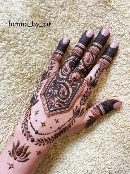 A full view of a bridal henna design with a central geometric shape filled with paisley motifs. The fingers are fully colored, and a leafy vine border completes the look.