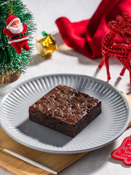 A simple brownie on a grey plate, surrounded by festive Christmas ornaments for a seasonal dessert special.