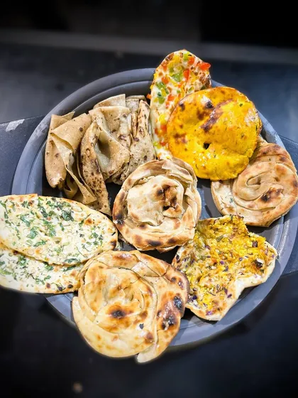 I offer a wide variety of freshly made Indian breads to accompany my main courses. This platter shows a selection including Lachha Paratha, Garlic Naan, and Missi Roti, ensuring there's something for everyone.