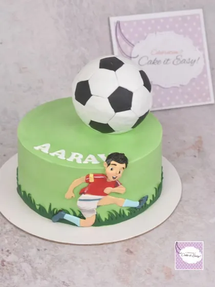 A simple football-themed cake with a 3D ball and a figurine of a player in action.