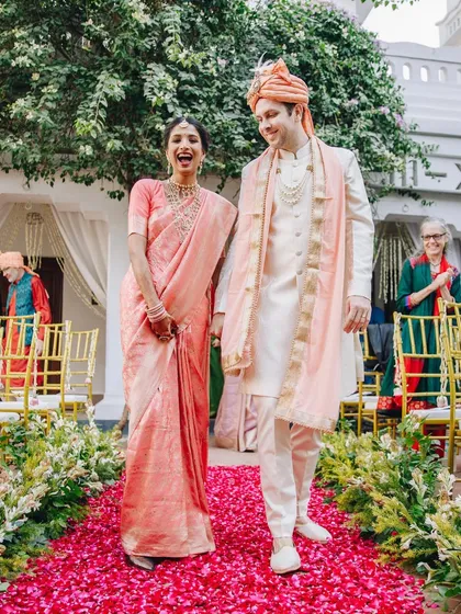 Pure, uninhibited joy. The bride's laughter lights up the aisle as she walks with her groom on a path of vibrant pink petals. This candid moment perfectly captures the happiness of a cross-cultural wedding celebration.