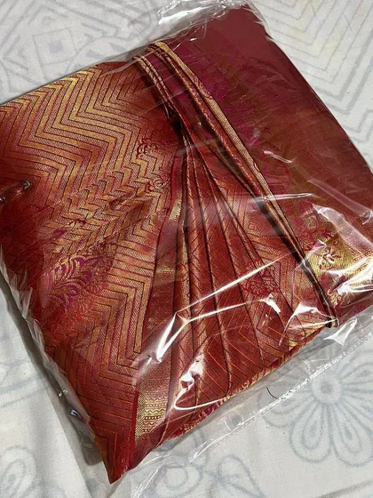 A close-up of a red silk saree, packed after box folding. The plastic cover protects it from dust and damage.