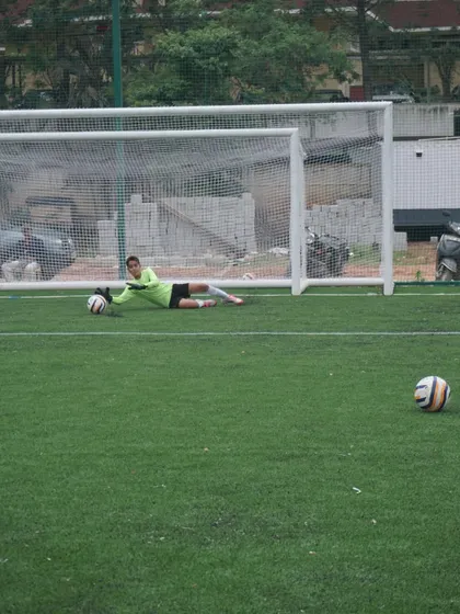A goalkeeper executes a perfect low diving save, securing the ball on the turf. This drill focuses on proper technique for handling shots aimed at the bottom corners of the goal.