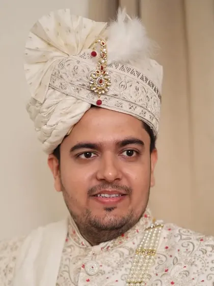A close-up of the groom's face, showing the subtle makeup and the intricate details of his turban. The look is clean, masculine, and polished.