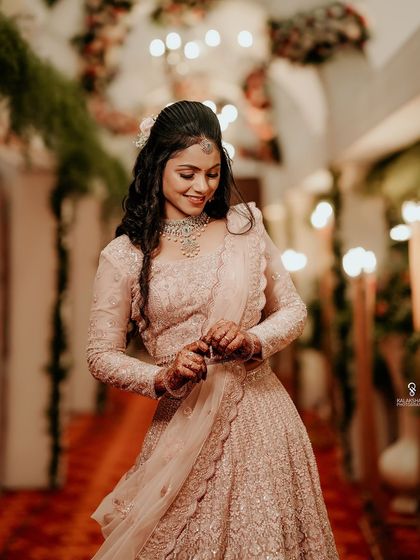 A smiling bride in a pink lehenga, captured in a beautifully lit hallway.