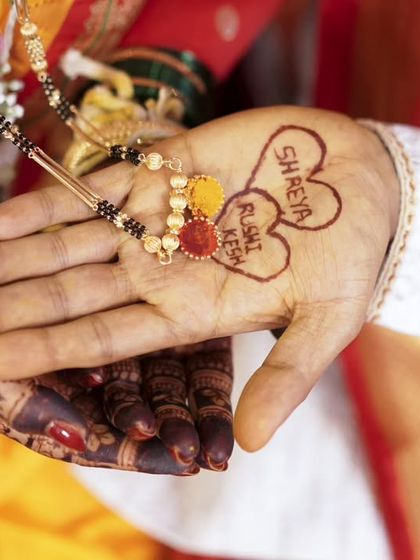 A creative detail shot showing the 'mangalsutra' and the couple's names written in henna on the groom's hand.