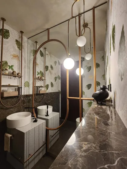 A closer look at the powder room's design, showcasing the interplay of materials. The cool marble of the vanity contrasts with the warm brass framing and the organic leaf-patterned wallpaper, creating a space that is visually rich and intriguing.