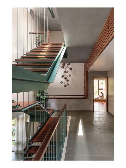 The main staircase is conceived as a sculptural object, with a prominent green steel stringer beam supporting floating wooden treads. This element acts as a strong visual marker that organizes the interior spaces around it.