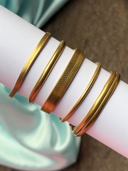 A close-up of our gold-plated stackable bracelets, including a flat herringbone chain and simple round bangles.