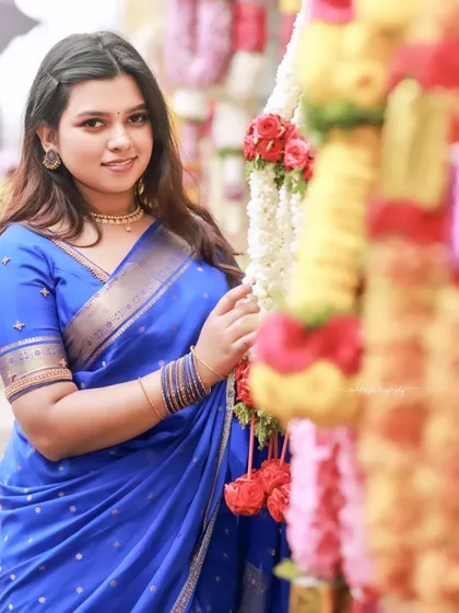 A festive shot with the bride standing next to colorful flower garlands, adding a celebratory feel to the temple setting.