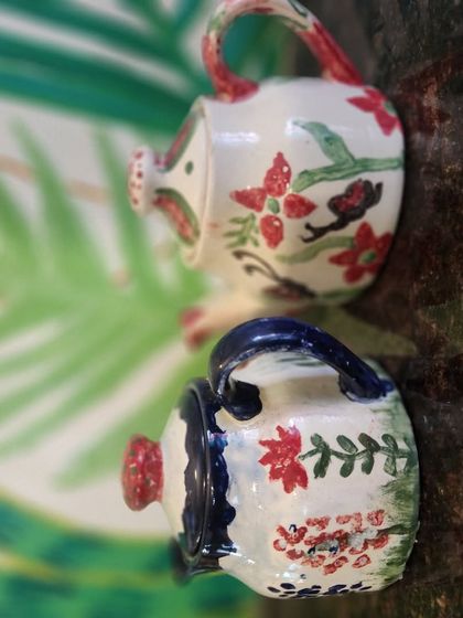 A pair of small, hand painted ceramic watering cans, decorated with delicate floral patterns. A great example of our DIY ceramic painting.