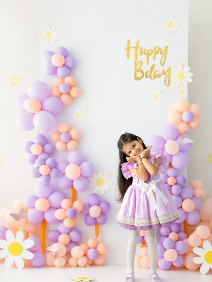 A playful pose to celebrate her special day. The custom balloon backdrop in her favorite colors makes this birthday photoshoot feel personal and fun.