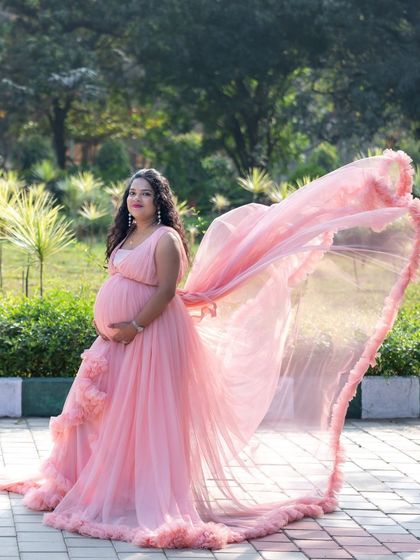 A dynamic shot of a mom-to-be in a pink gown with a flowing train in a park setting.