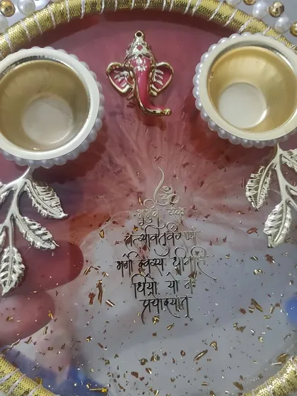 This is a close-up of a custom Pooja thali, perfect for wedding ceremonies or your home mandir. I used a rich red and white resin base with gold flakes, adding a Ganesha charm, a Sanskrit shloka, and holders for roli and chawal. The pearl and gold leaf border makes it a truly special piece for any auspicious occasion.