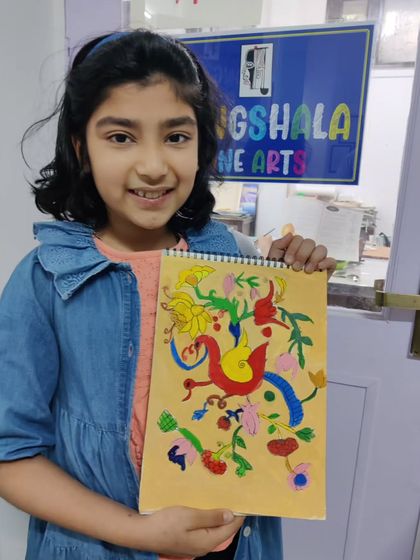 A young student proudly displays her completed folk art painting, filled with colorful and imaginative birds and flowers.