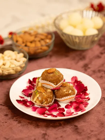 A festive shot of traditional Indian sweets (laddoos) for Diwali. The composition includes other festive elements like nuts and rose petals.