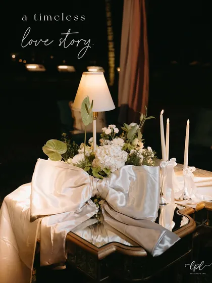 A table centerpiece with a lamp and a large silver bow, with the text overlay "a timeless love story".