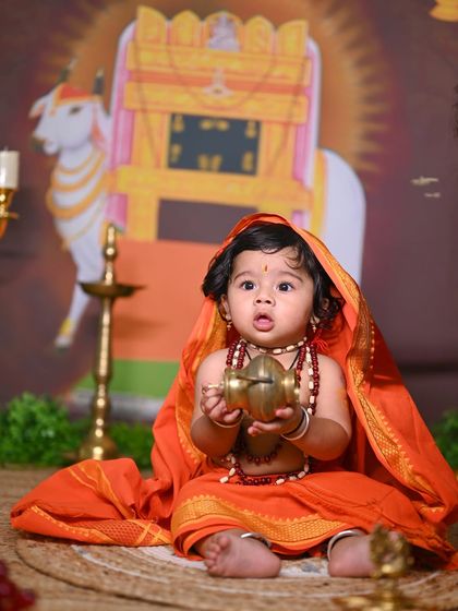 A toddler dressed as Raghavendra Swamy, curiously holding a small pot.