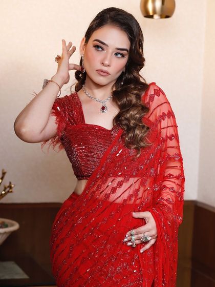 This pose highlights the sheer fabric and sequin details of the red draped saree, a perfect choice for a reception or party.