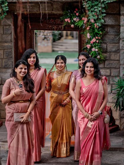 A bride and her bridesmaids, all dressed in beautiful sarees, pose for a group photo against our stone walls.
