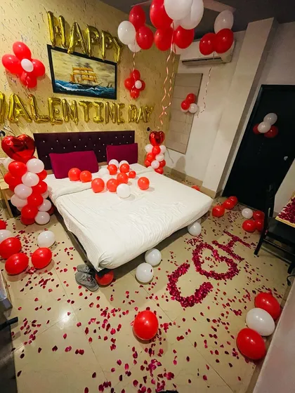 Perfect for Valentine's Day, this decoration uses classic red and white balloons to fill the room with love. The design includes "Happy Valentine Day" foil letters and initials spelled out with rose petals on the floor.