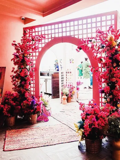 A vibrant pink floral entrance for a daytime Mehendi. The arched trellis and bright bougainvillea create a cheerful and welcoming entryway for guests.