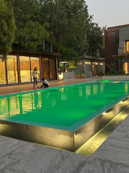 The infinity-edge swimming pool with custom green lighting at night. The pool is a central feature of the landscape design, creating a tranquil and visually striking focal point.