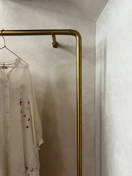 A detail of a simple brass clothing rod against the textured wall finish at Eka. The minimalist fixture allows the delicate, handcrafted clothing to be the main focus.