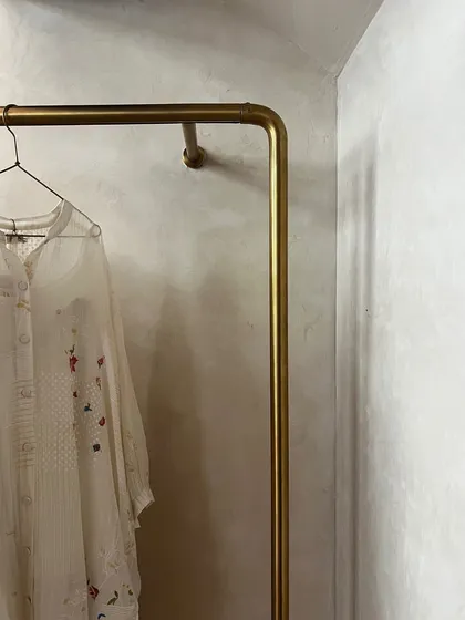 A detail of a simple brass clothing rod against the textured wall finish at Eka. The minimalist fixture allows the delicate, handcrafted clothing to be the main focus.