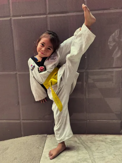 This young girl with a yellow belt shows off her high kick and a big smile. This is what girl power and dedication look like.
