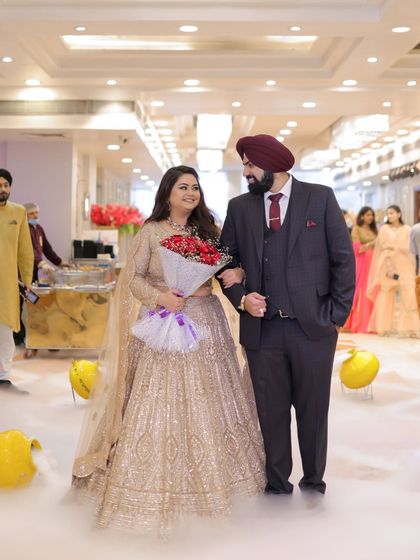 The grand entrance. Ishita, holding a bouquet of red roses, walks in with Dipender, surrounded by the warm glow of their celebration and plumes of dry ice.