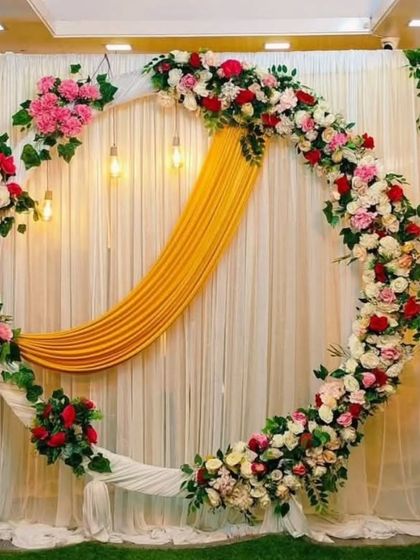A unique circular backdrop with an asymmetrical floral design. The combination of white, pink, and red roses with a pop of yellow drape creates a modern and artistic look.