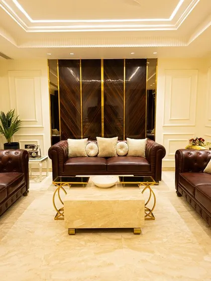 A classic living room setup with rich brown leather chesterfield sofas. The high-gloss wood paneling and elegant white walls with gold accents create a timeless and luxurious feel.
