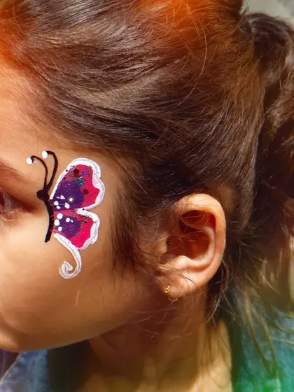 A delicate butterfly design painted on a child's cheek, showing how even a small painting can add a lot of fun to the party look.