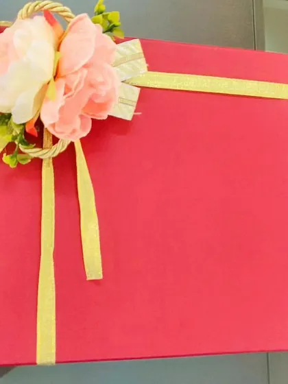 An elegant, simple red gift box tied with a golden ribbon and a floral arrangement, perfect for any occasion.