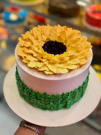 A stunning sunflower cake with a large, detailed buttercream sunflower on top. The design is bright, cheerful, and a true work of art for any celebration.