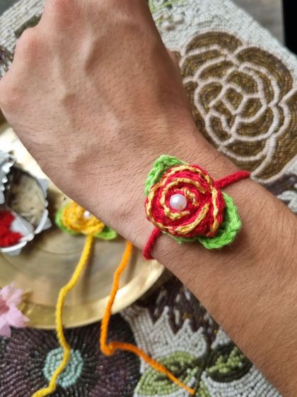 This detailed rose rakhi looks stunning when worn. The layered petals and pearl center make it a truly special piece.