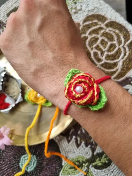 This detailed rose rakhi looks stunning when worn. The layered petals and pearl center make it a truly special piece.