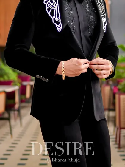 A detail shot of the black velvet blazer being buttoned. Every element, from the fabric to the embroidery, is chosen for its quality and impact.