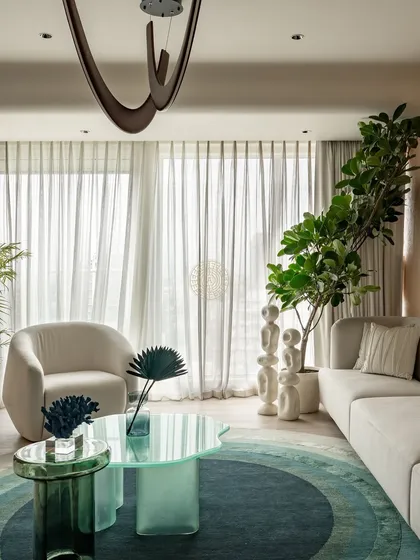 A mix of textures and materials defines this living space. A translucent green coffee table adds a pop of color, while the neutral tones of the sofa and armchair create a calm and serene atmosphere.