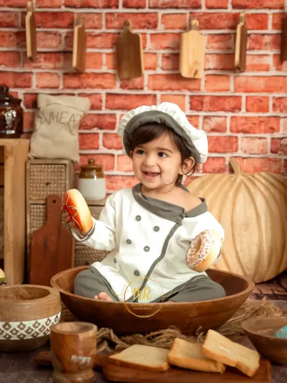 A happy 'Little Chef' sitting in a large wooden bowl, holding toy donuts with a huge smile.