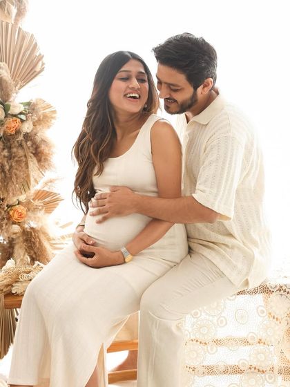 A playful and loving interaction during a boho-themed maternity shoot. The earthy tones and textures of the studio setup complement the couple's relaxed and happy vibe.