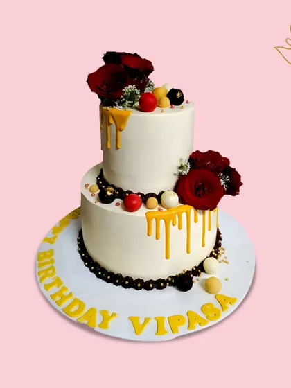 A stunning two-tier drip cake for Vipasa's birthday, adorned with red roses and gold drips. This elegant creation is perfect for a glamorous celebration.