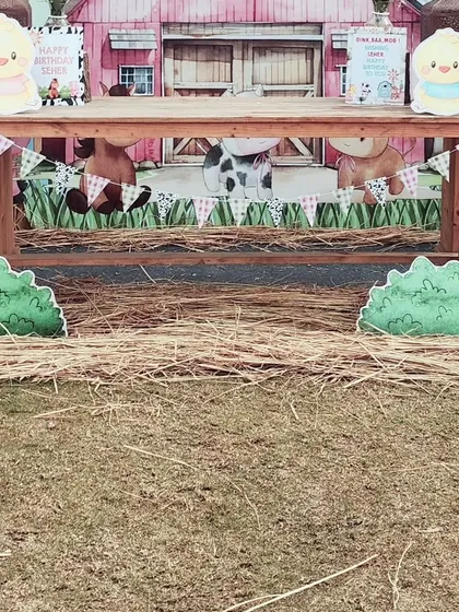 The main cake table setup for the farm party. A rustic wooden table is set in front of the barn backdrop, with hay bales and animal cutouts creating a complete barnyard scene.
