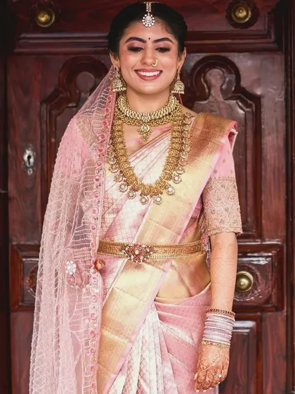 A bride in a soft pink Kanchipuram saree. Her custom blouse is fully embroidered with intricate patterns, creating a look of timeless elegance for her wedding day.