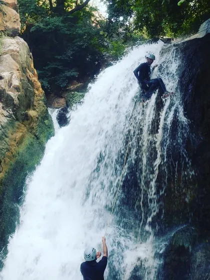 A student confidently navigating the rock face alongside the waterfall, using her feet to maintain a stable position.