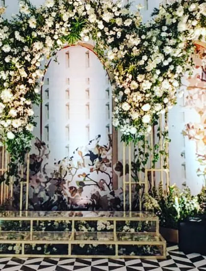 This reception stage features beautiful printed backdrops inside floral arches. The design combines the elegance of white roses with artistic patterns for a sophisticated and unique look.